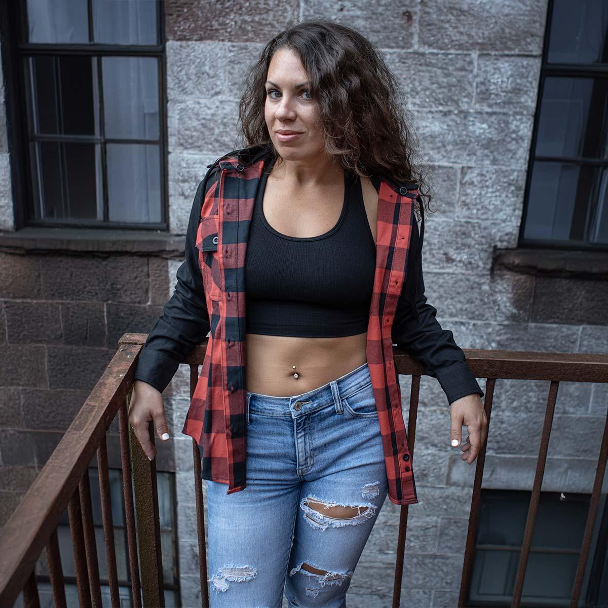 Woman in black crop top and red plaid shirt posing on stairs, wearing ripped jeans
