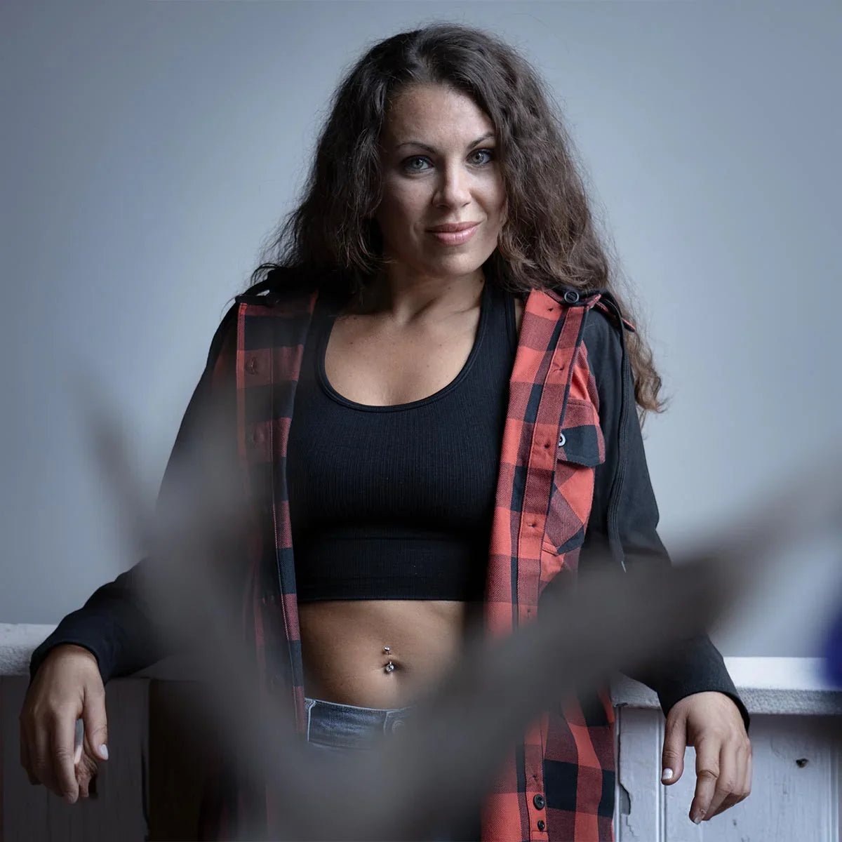 Woman in a black crop top and red plaid shirt posing indoors with casual style