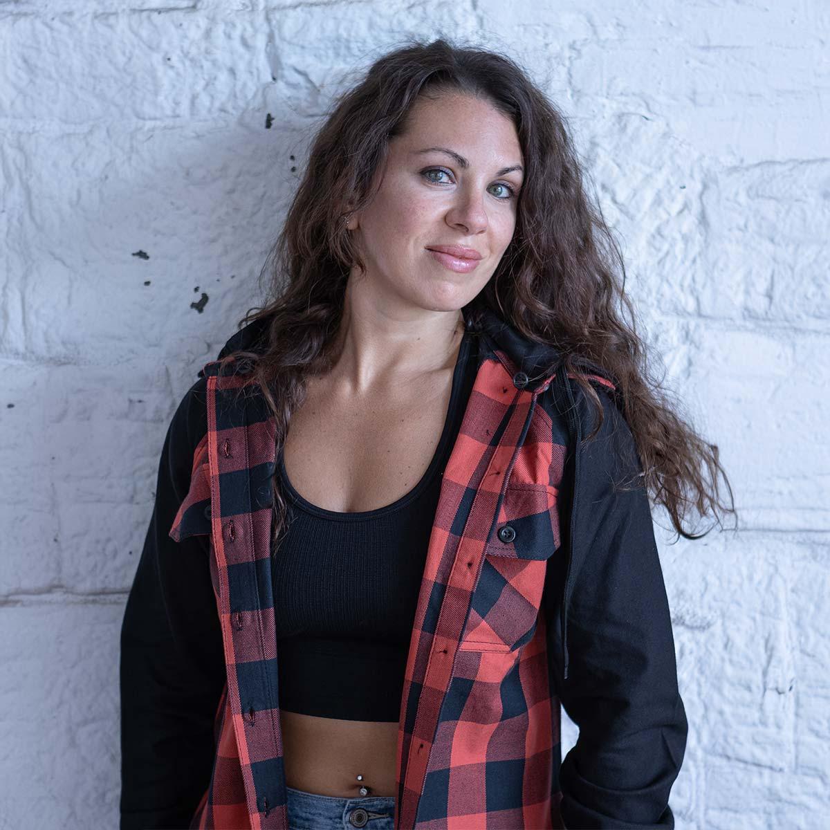 Woman in red plaid jacket and black crop top standing against a white brick wall