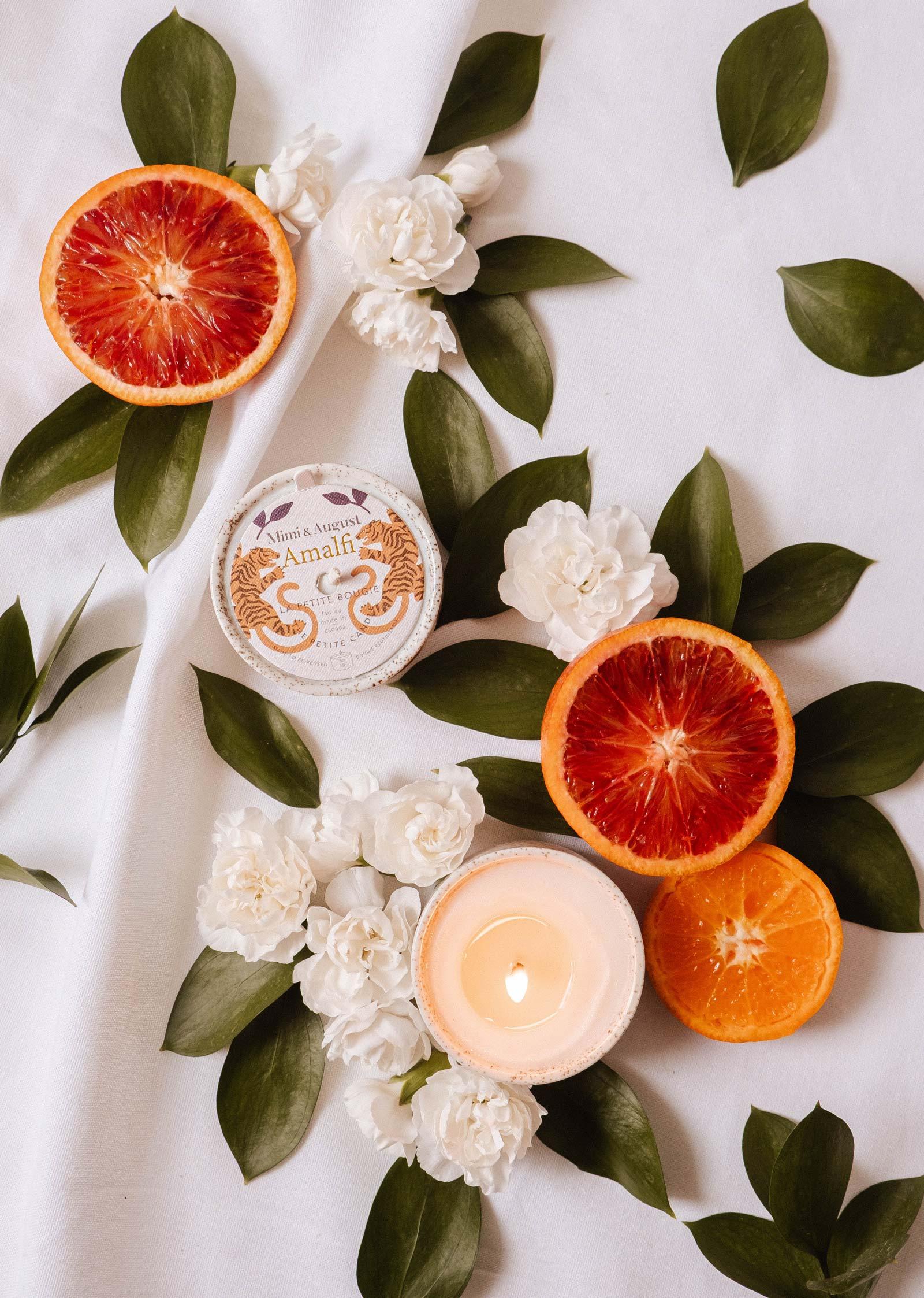 Amalfi reusable candle with floral accents, sliced blood orange, and green leaves on white fabric