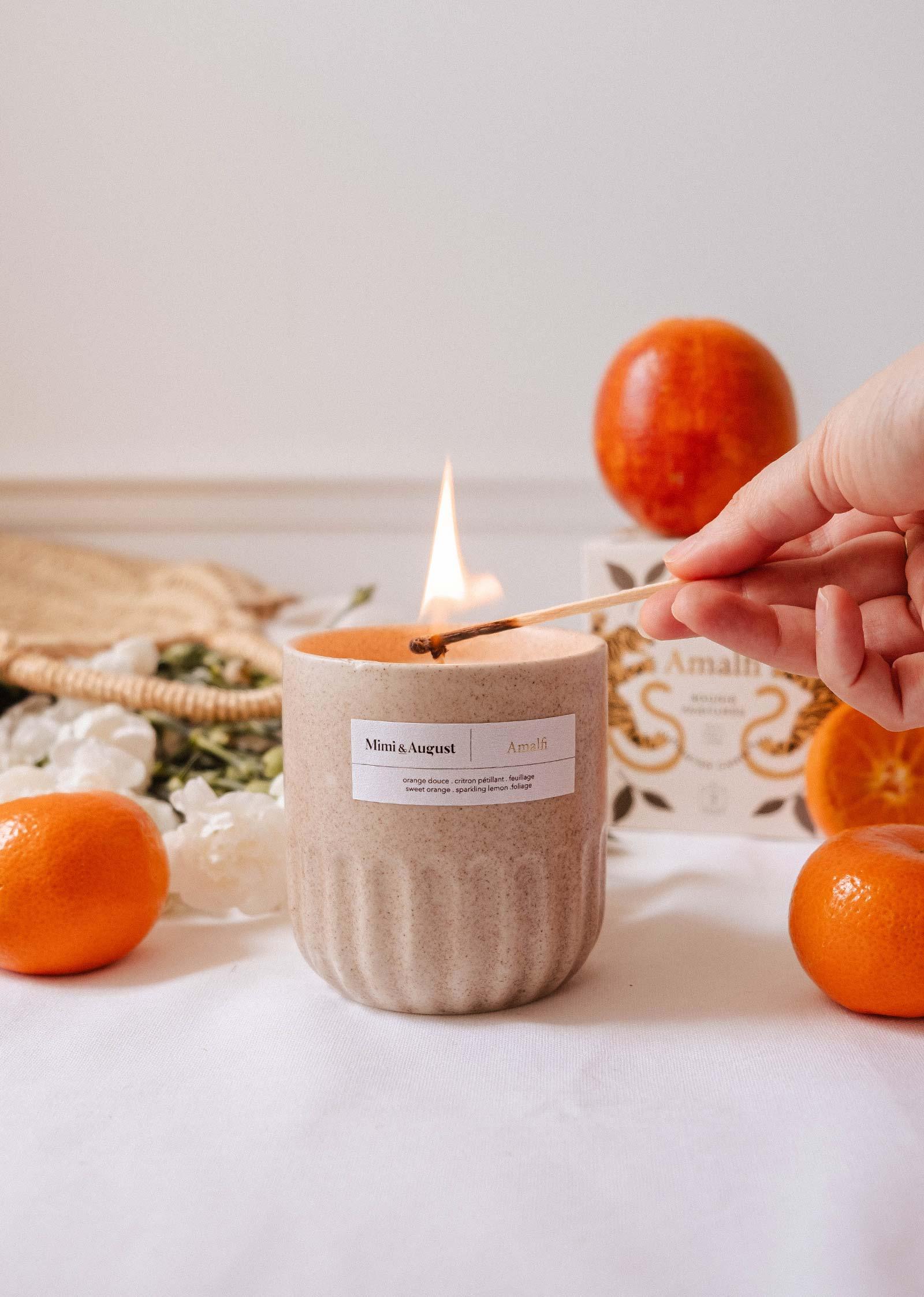 Hand lighting Mimi & August Amalfi reusable candle with oranges and flowers nearby