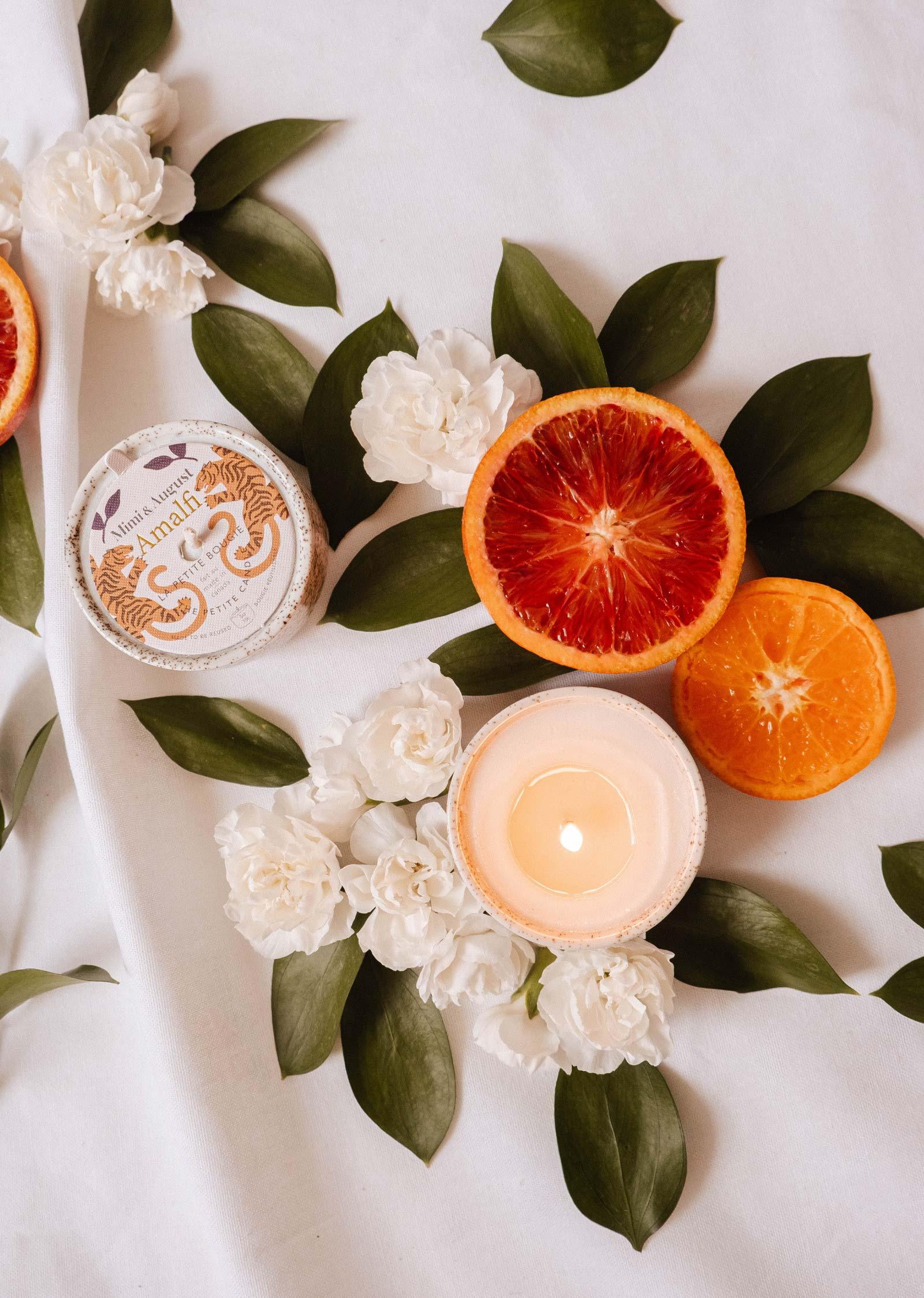 Amalfi reusable candle with white flowers, green leaves, and sliced citrus on white fabric