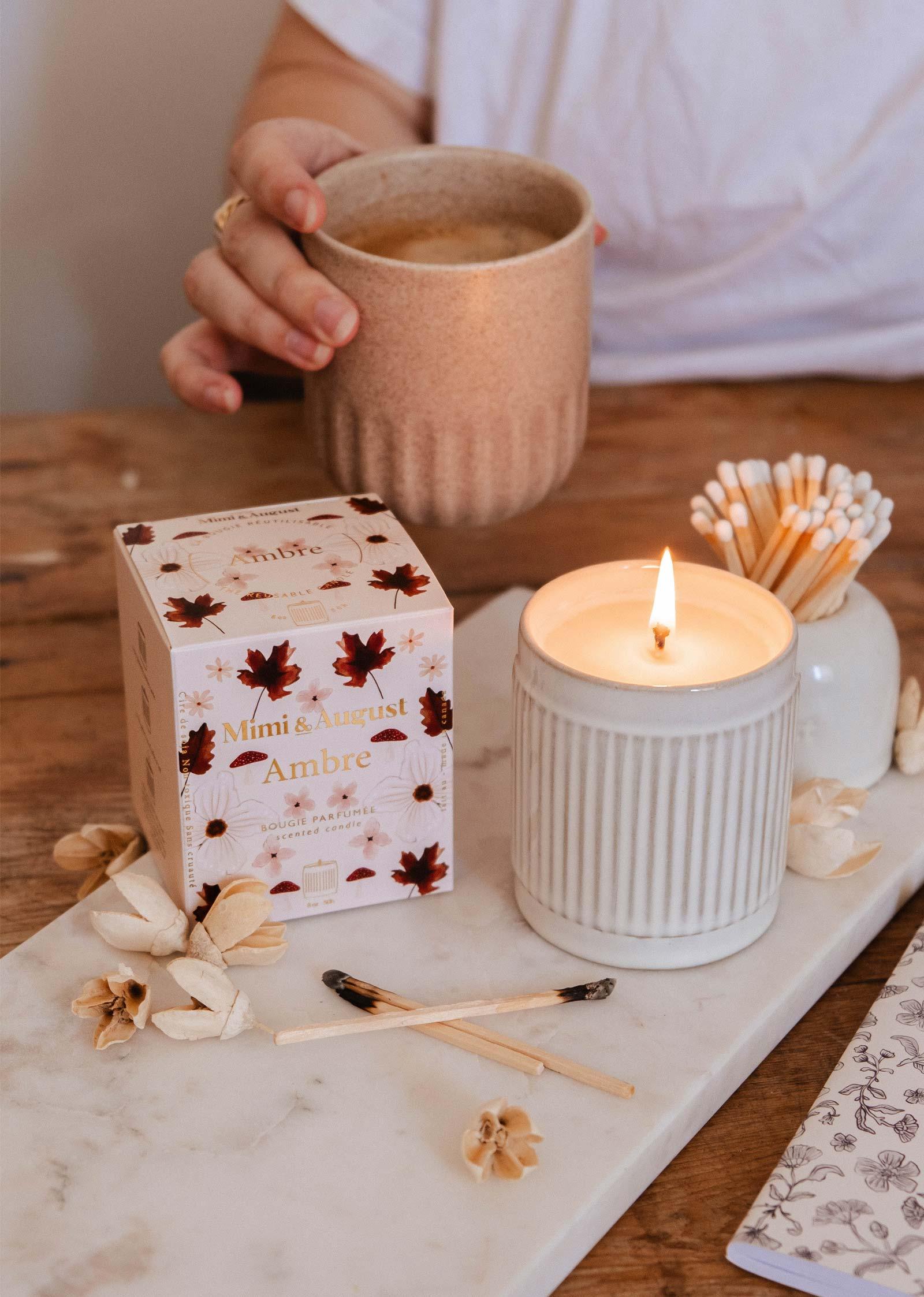 Mimi & August Ambre soy wax candle in a ribbed jar beside floral box and person holding mug