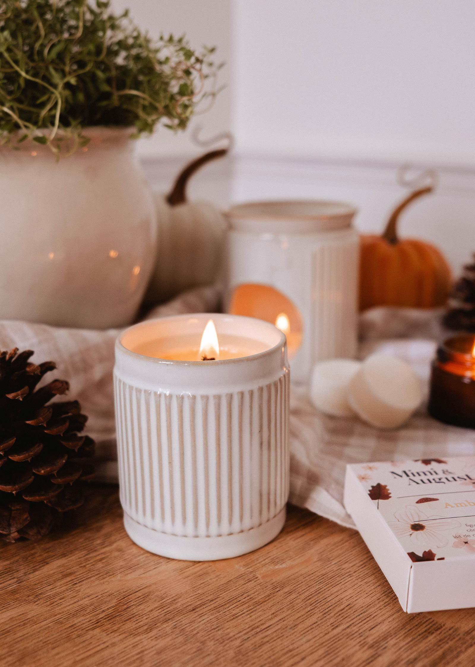 Amber soy wax candle in ceramic jar on wood table with pumpkins and pinecones, cozy decor