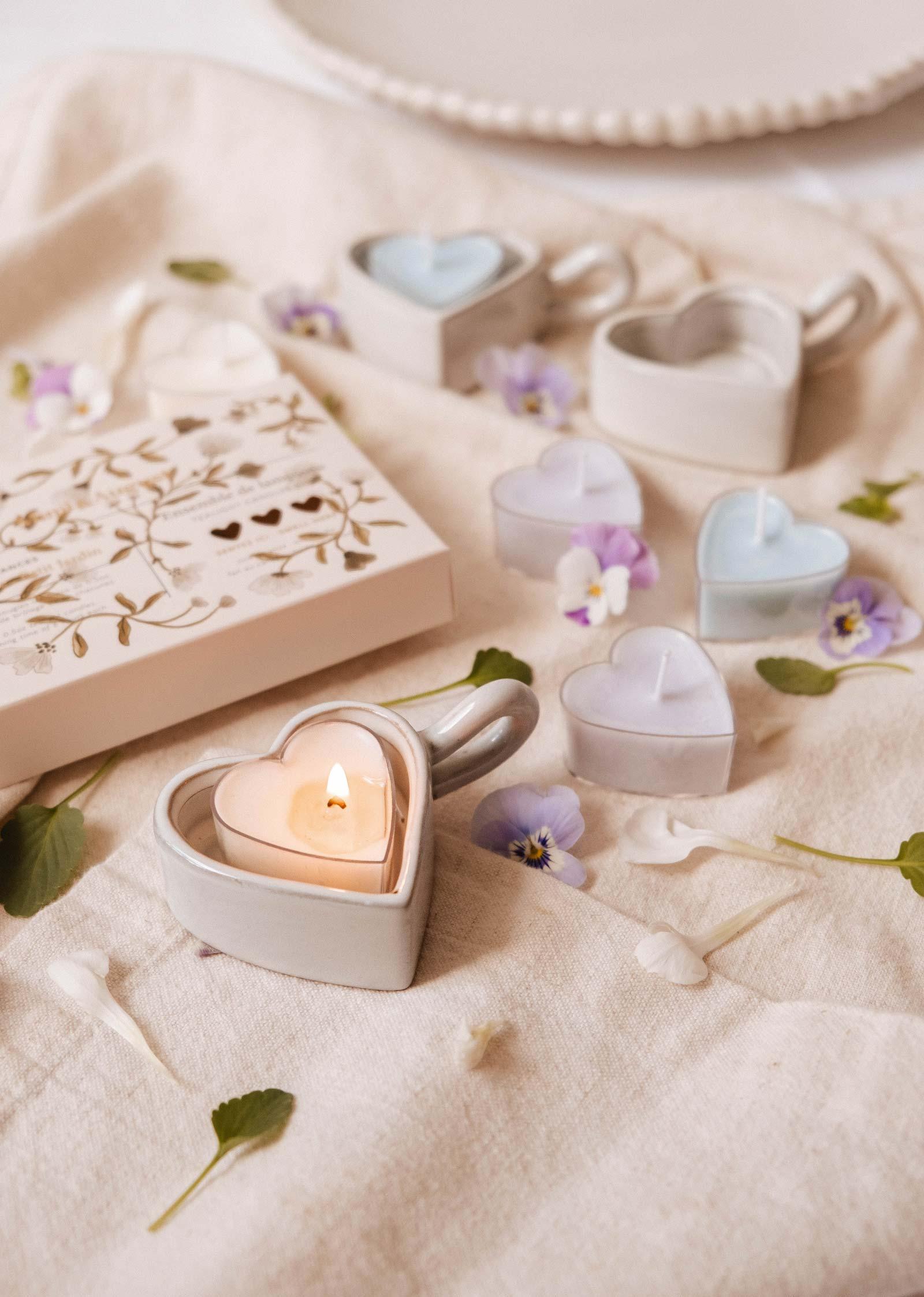 Heart-shaped tealight candles in ceramic holders with flowers on a soft beige cloth.