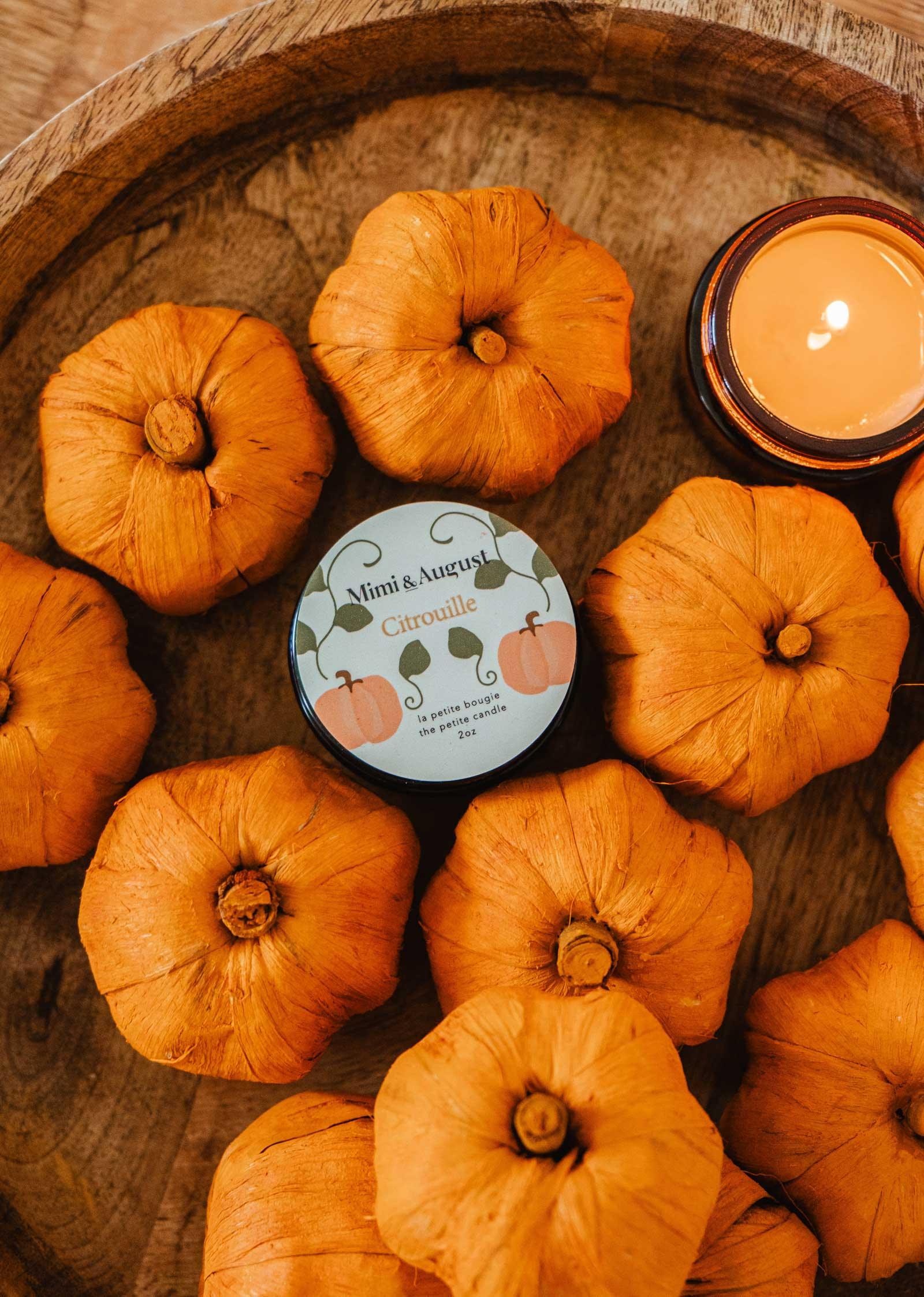 Citrouille reusable candle by Mimi & August surrounded by small orange pumpkins in a wooden bowl