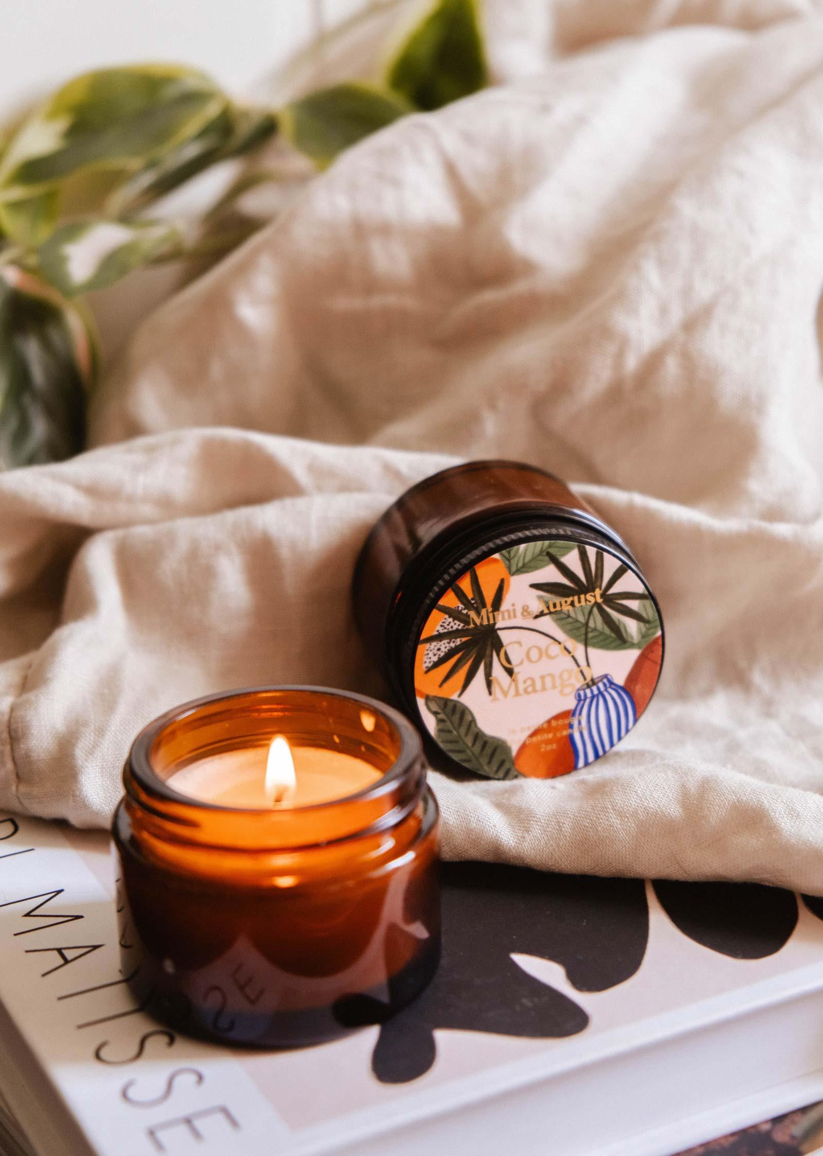 Coco Mango mini candle in amber jar by Mimi & August on linen with a book and plant
