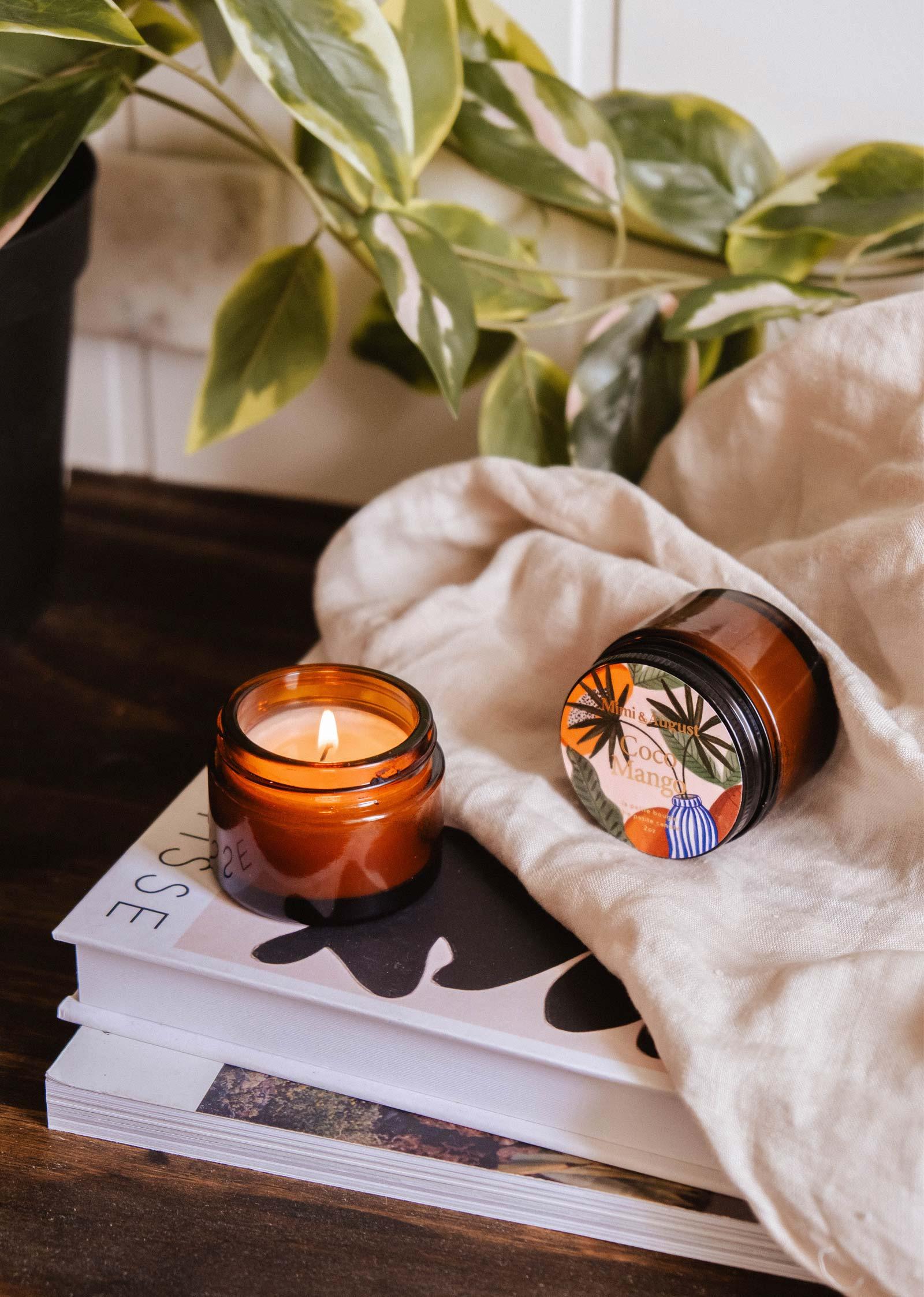 Coco Mango mini candle in amber jar by Mimi and August on books beside a plant