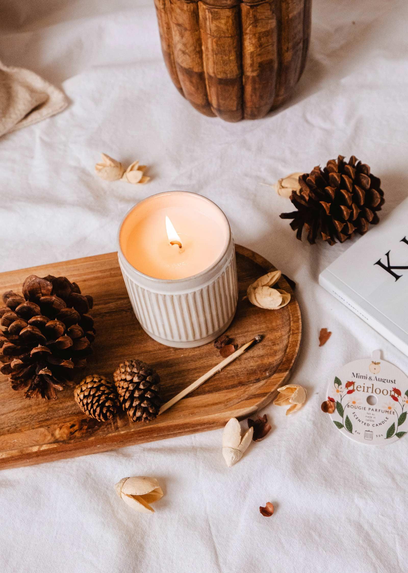 Heirloom reusable candle by Mimi and August on wooden tray with pinecones and cozy decor.