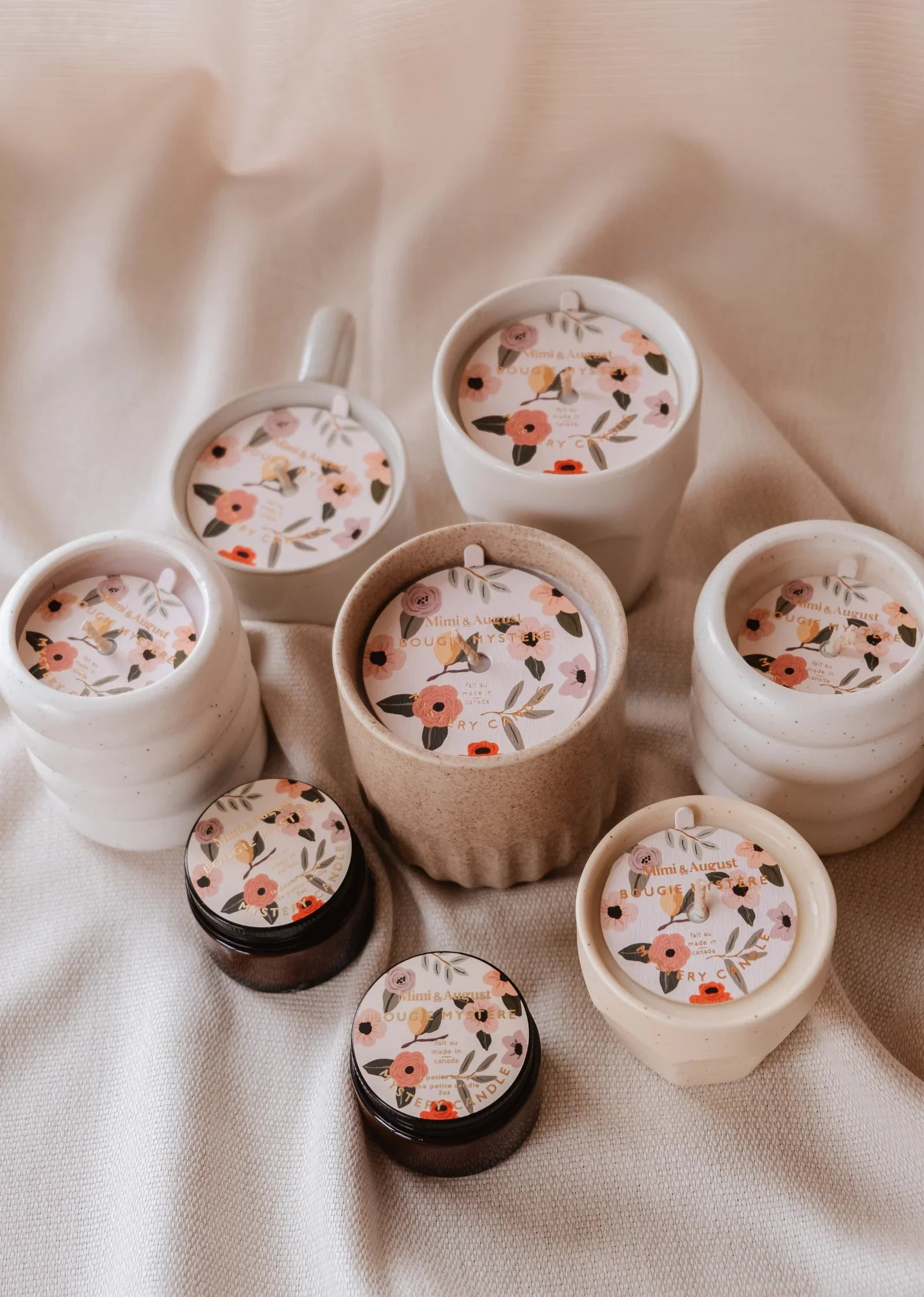 Assorted floral label candles in ceramic and glass jars on beige fabric