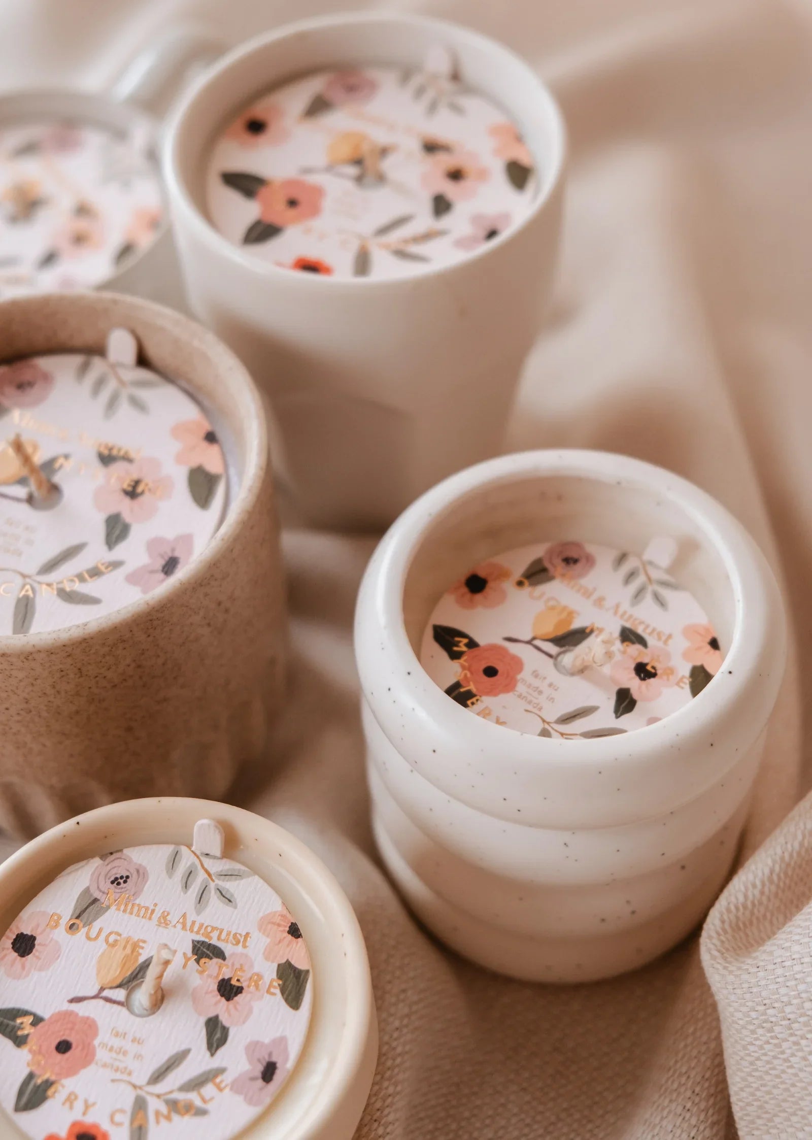 Ceramic candles with floral labels on a soft beige fabric, cozy home decor.