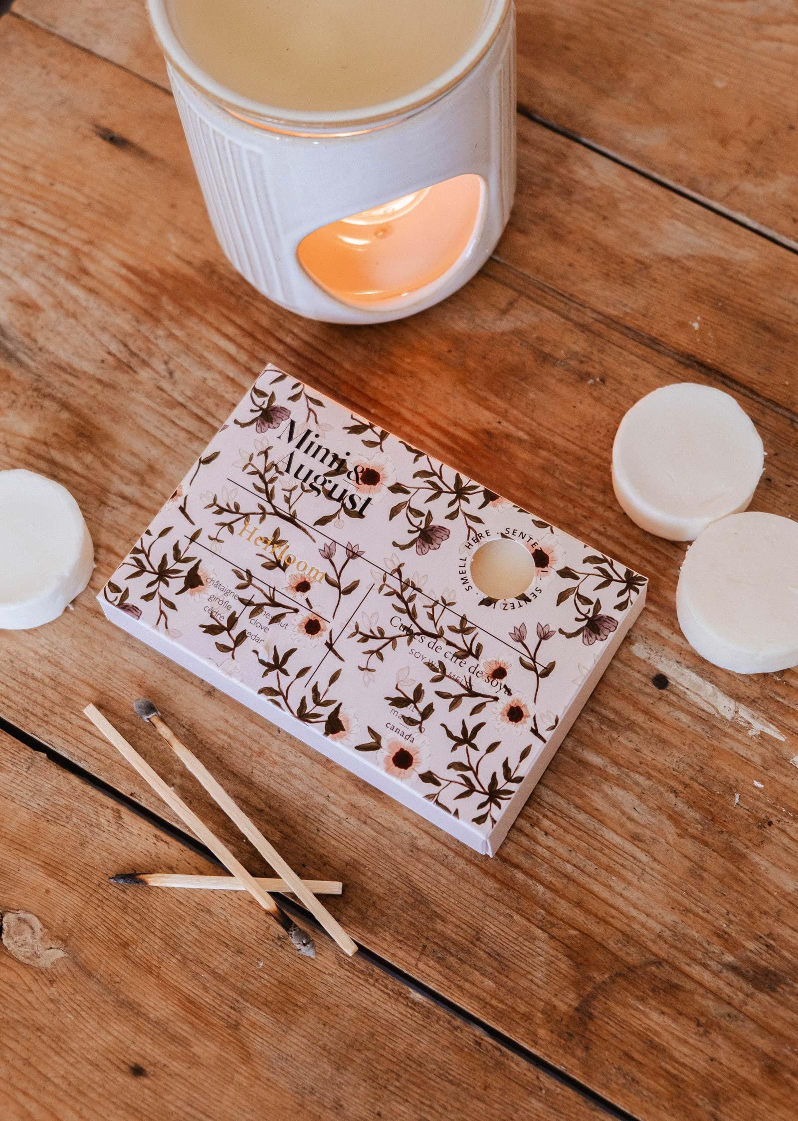 Heirloom soy wax melts by Mimi & August with matches and a lit wax warmer on wood table.