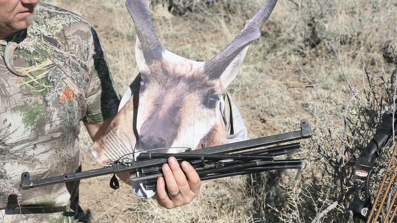 Man in camo shirt holds antelope decoy and frame in dry grassy outdoor setting