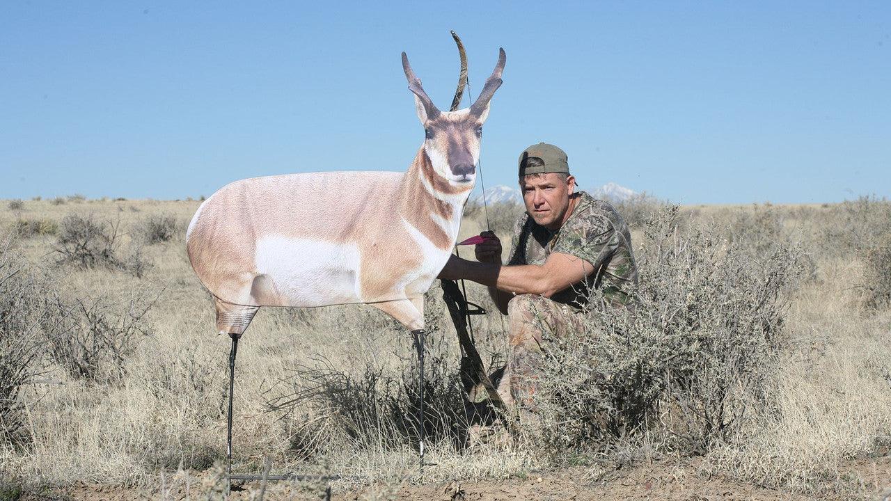 Hunter in camouflage crouching beside antelope decoy in dry grassland
