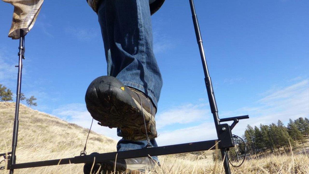 Close-up of person in jeans using an antelope decoy on grassy hill under blue sky