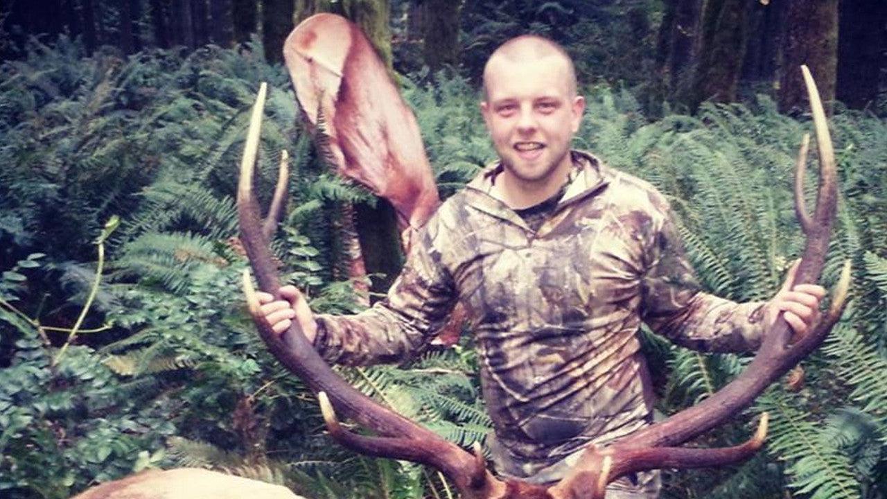 Man with camo jacket holding feeding elk decoy with antlers in a forest setting