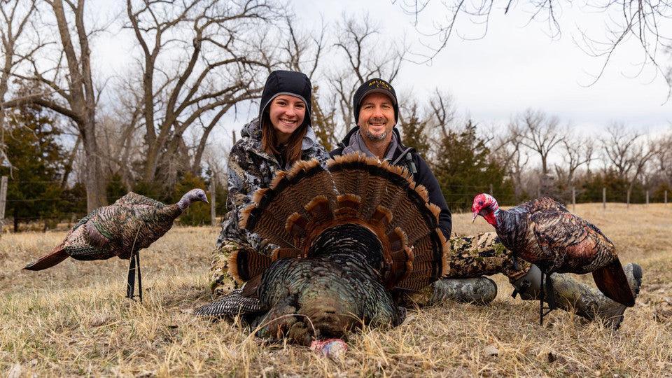 Two hunters posing with a harvested turkey and Montana turkey decoys outdoors in a field