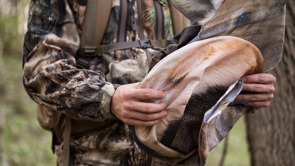 Hunter in camo holding folded elk decoy outdoors in the forest