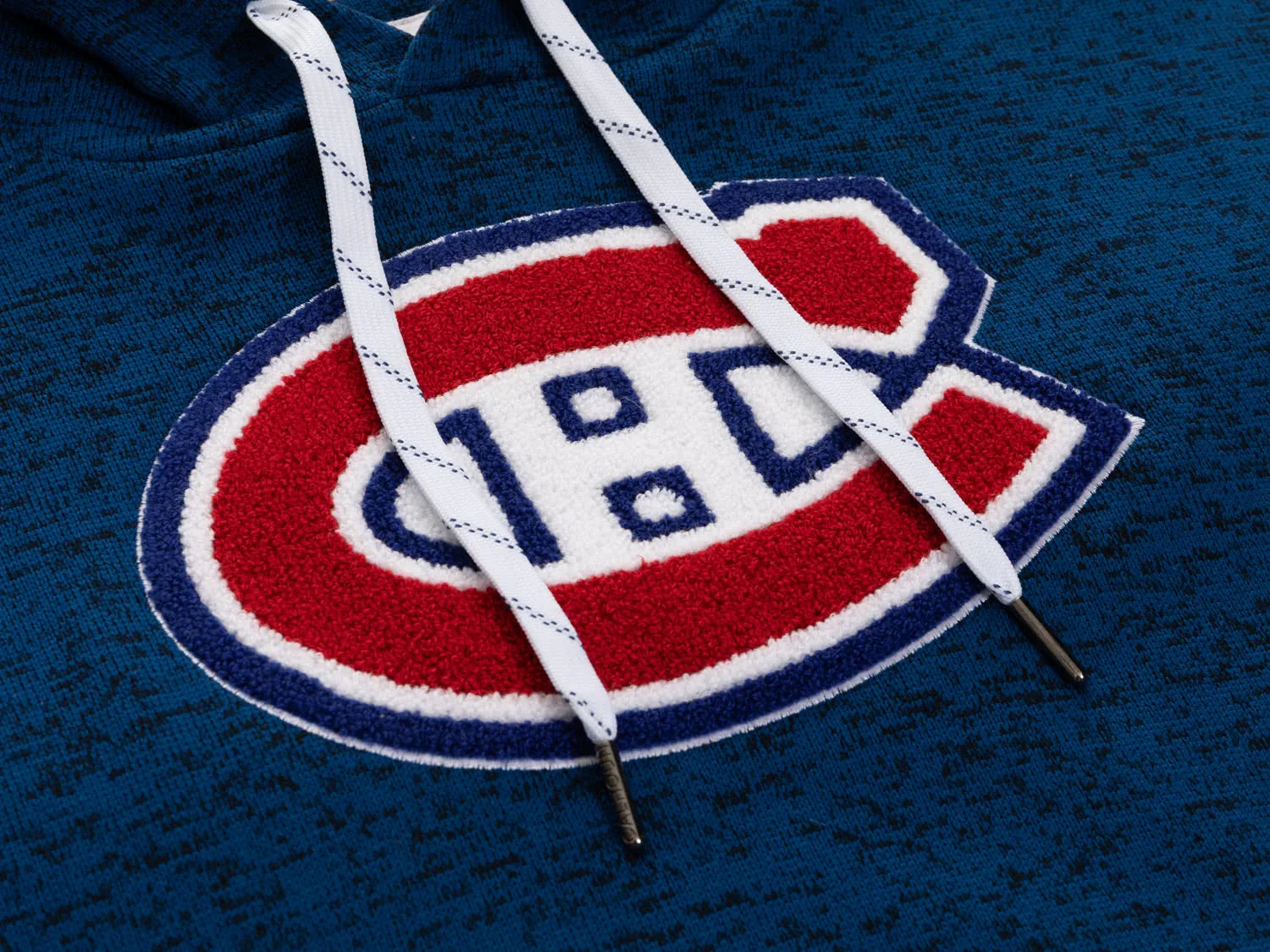 Montreal Canadiens logo patch on blue hoodie with white drawstrings, close-up detail