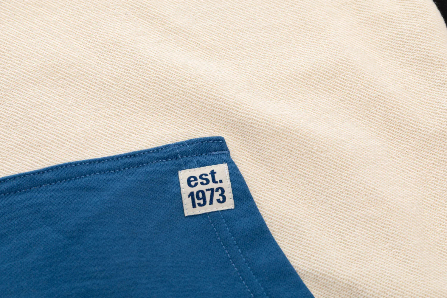 Cream knit hoodie fabric with blue trim and est. 1973 label detail