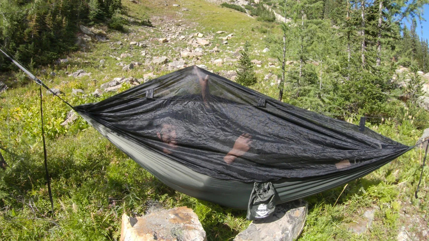 Camping hammock with mosquito net set up in a forested mountain area