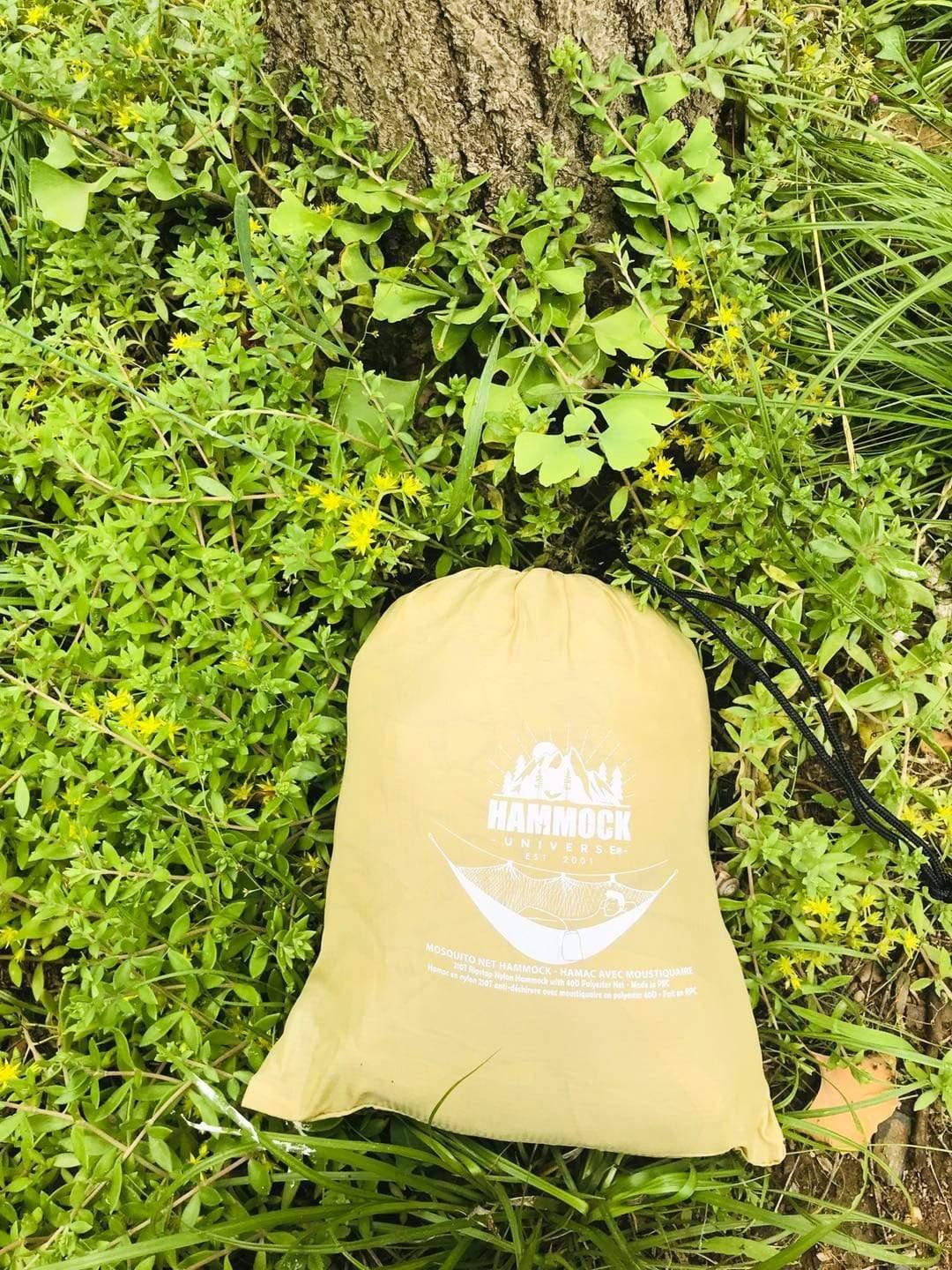 Hammock storage bag on grass near tree trunk, outdoor camping gear closeup