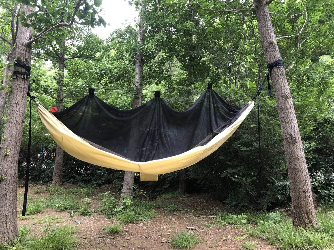 Yellow hammock with black mosquito net hanging between trees in a green forest setting
