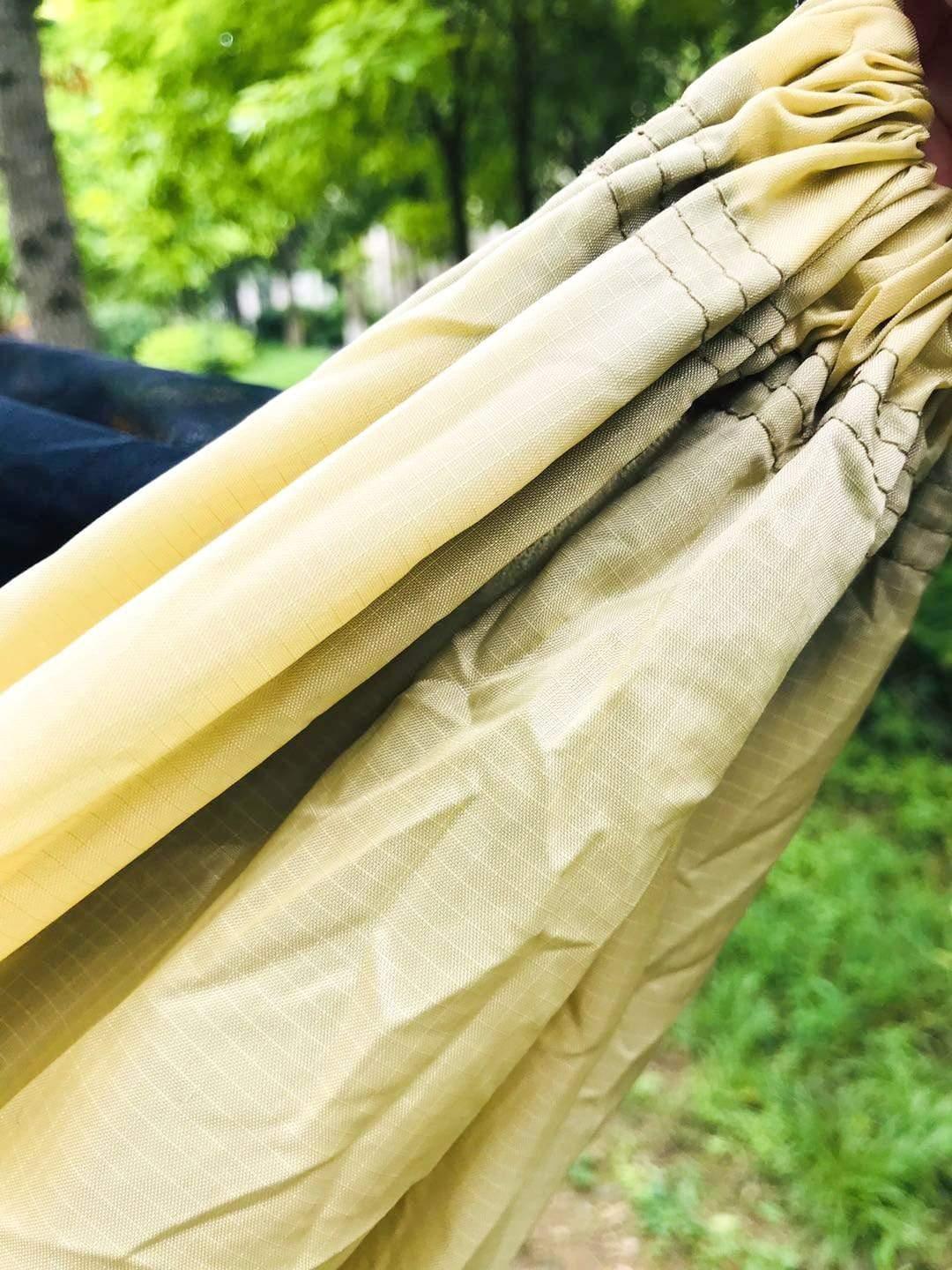 Close-up of yellow camping hammock fabric outdoors near green trees