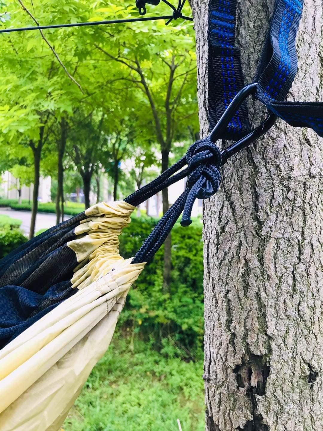 Hammock with nylon straps tied to tree outdoors in green forest park setting