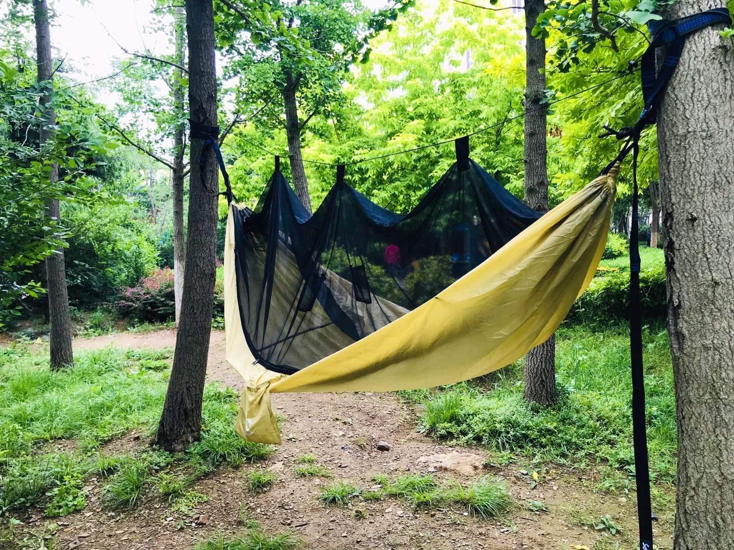 Yellow hammock with black mosquito net hanging between trees in a green forest setting