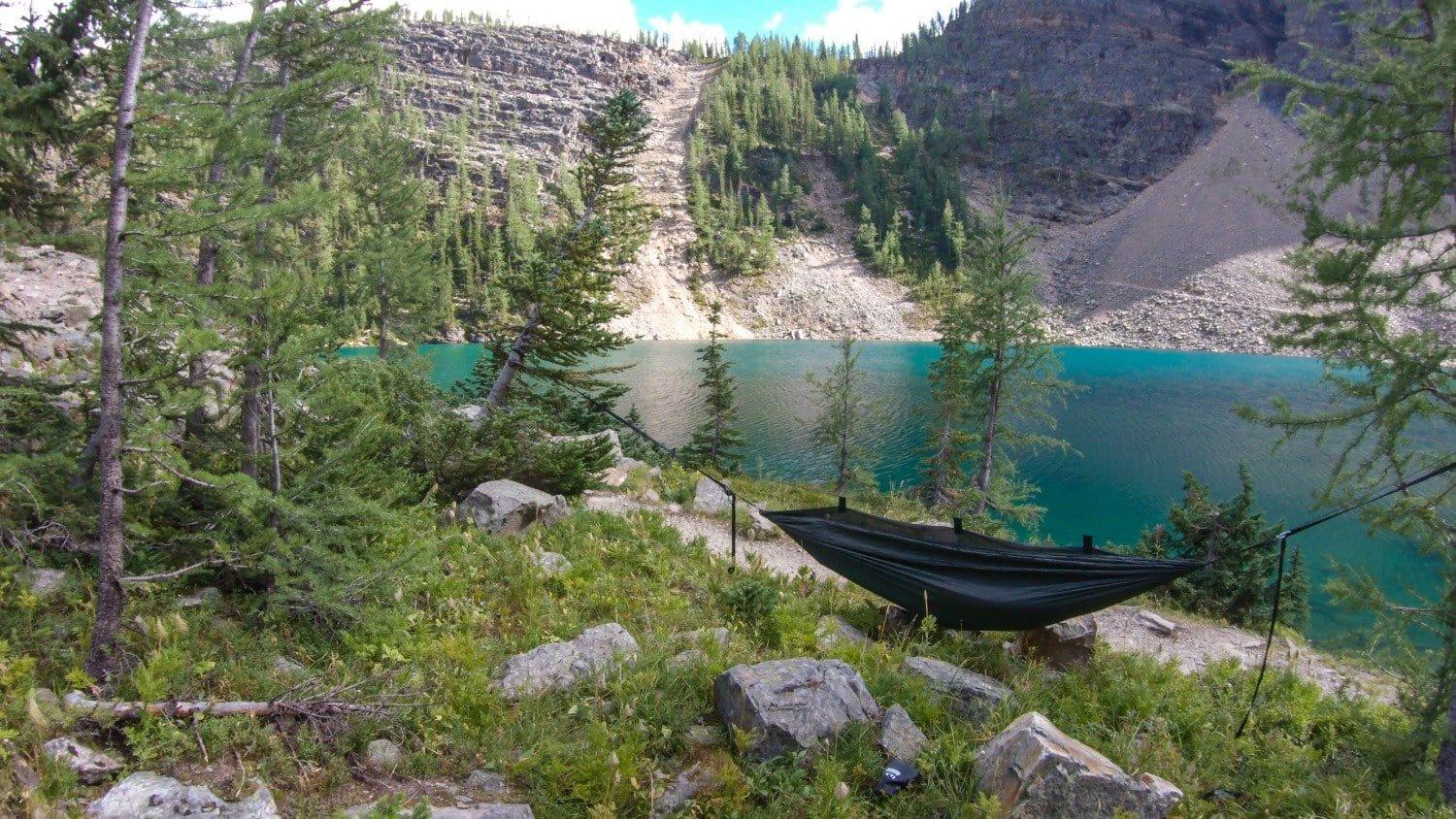 Camping hammock by turquoise mountain lake surrounded by pine trees and rocky landscape
