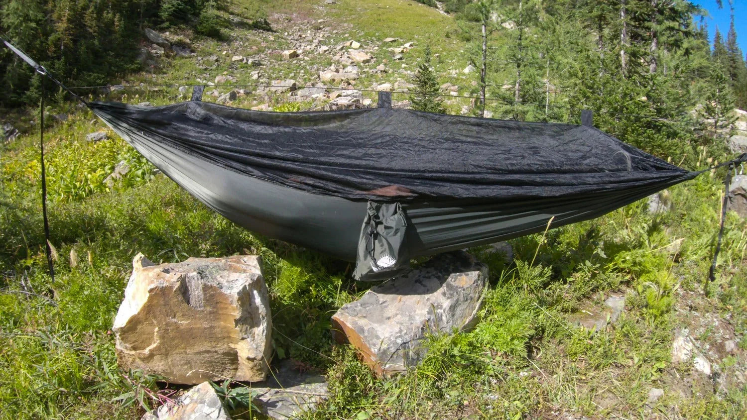 Camping hammock with mosquito net set up outdoors in a green mountain forest
