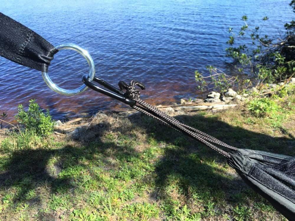Dark green hammock with metal ring and carabiner by a lakeside in nature