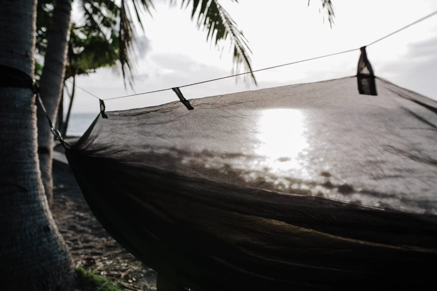 Black hammock with mosquito net under palm trees on a tropical beach at sunset