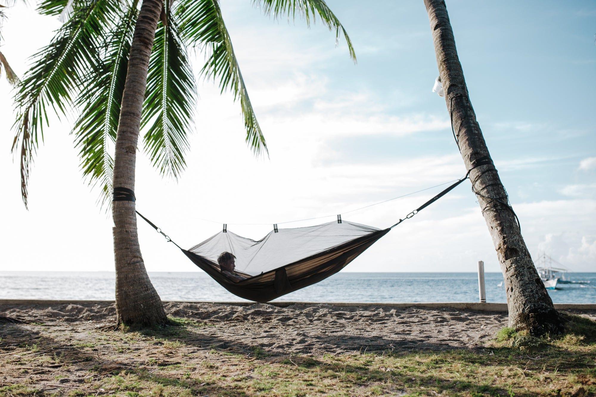 Person relaxing in a hammock with mosquito net between palm trees on a tropical beach
