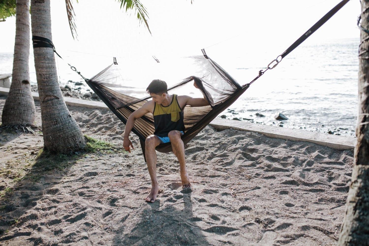 Man in mesh hammock on tropical beach with palm trees by the ocean
