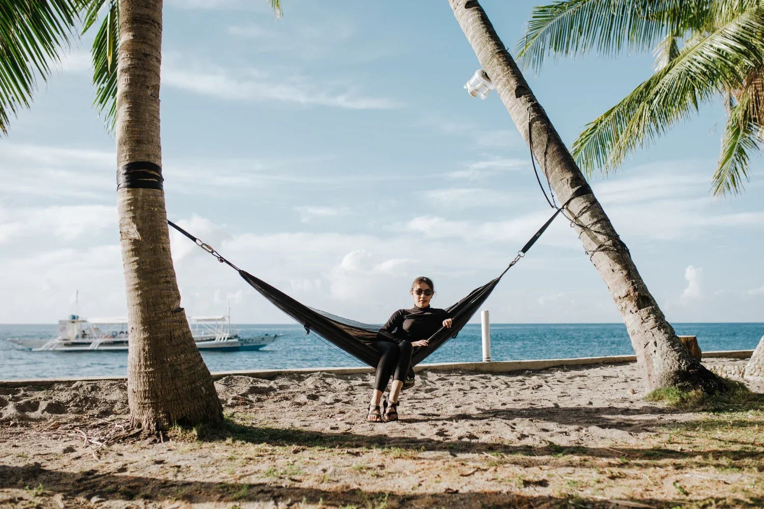 Woman relaxing in a hammock between palm trees on a tropical beach with ocean view