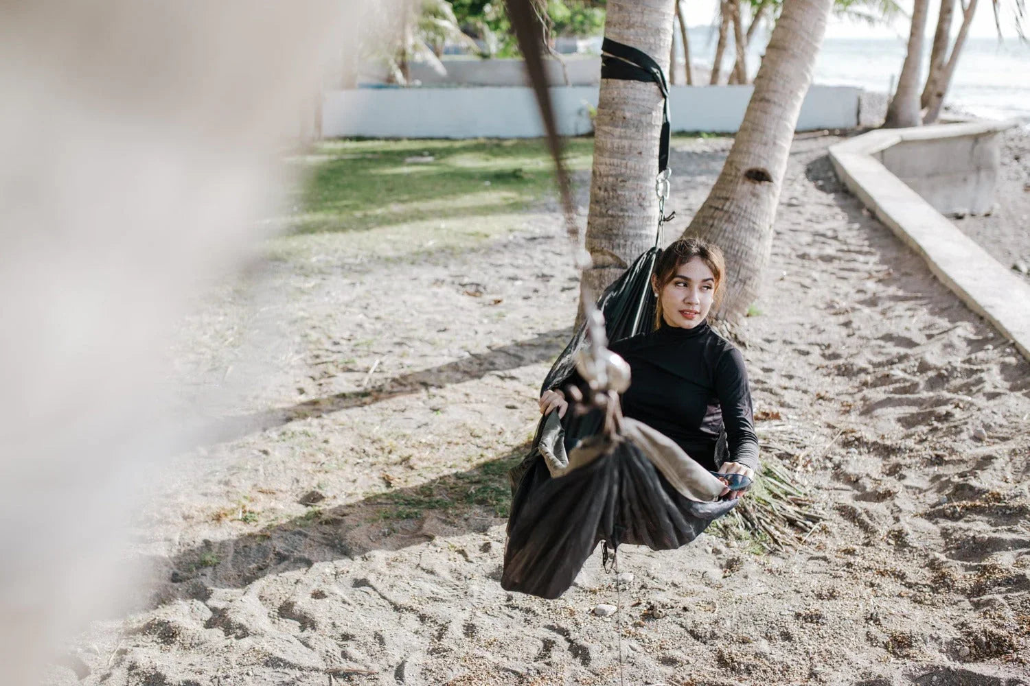 Woman relaxing in a hammock tied to palm trees on a sandy beach
