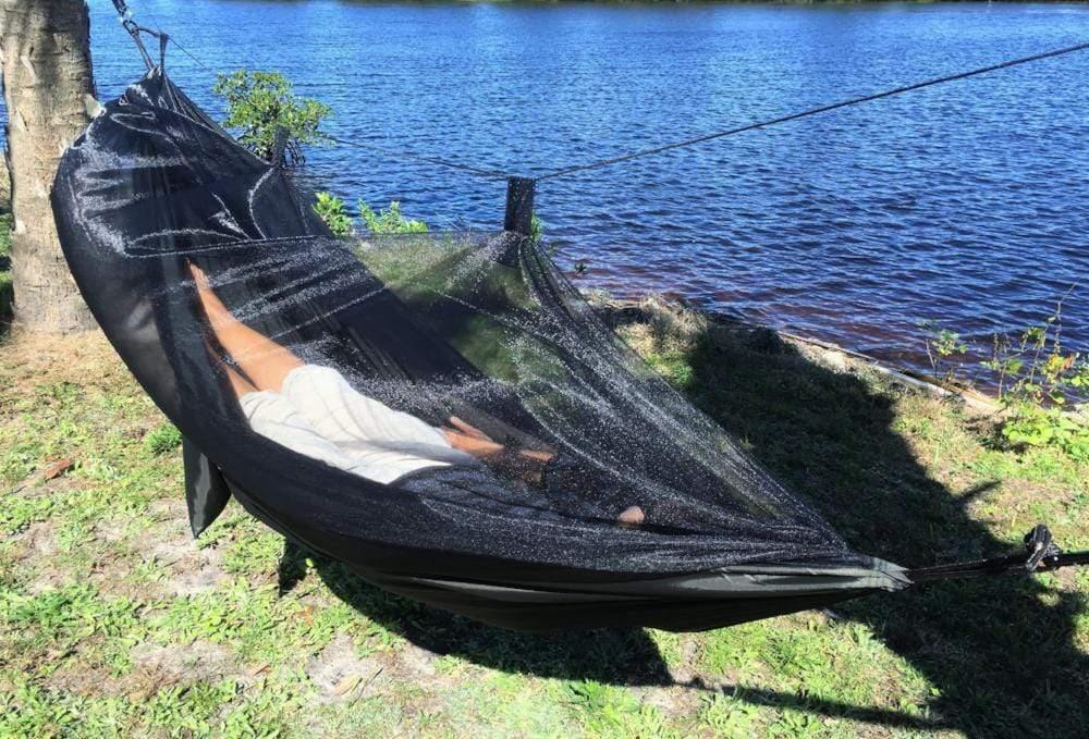 Dark green hammock with mosquito net by lakeside with person relaxing outdoors