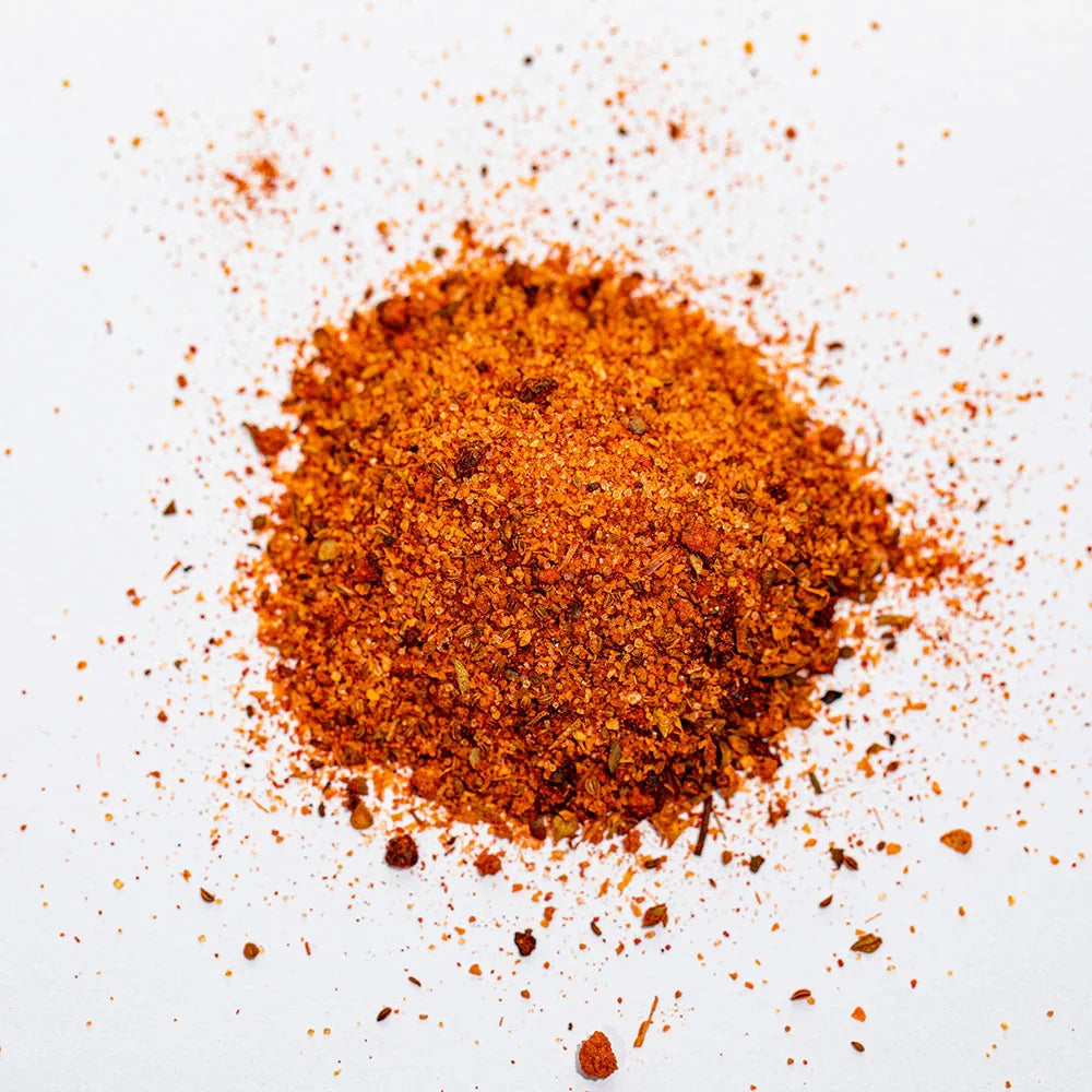 Pile of all-purpose seasoning blend on white background, vibrant orange-red color, spices