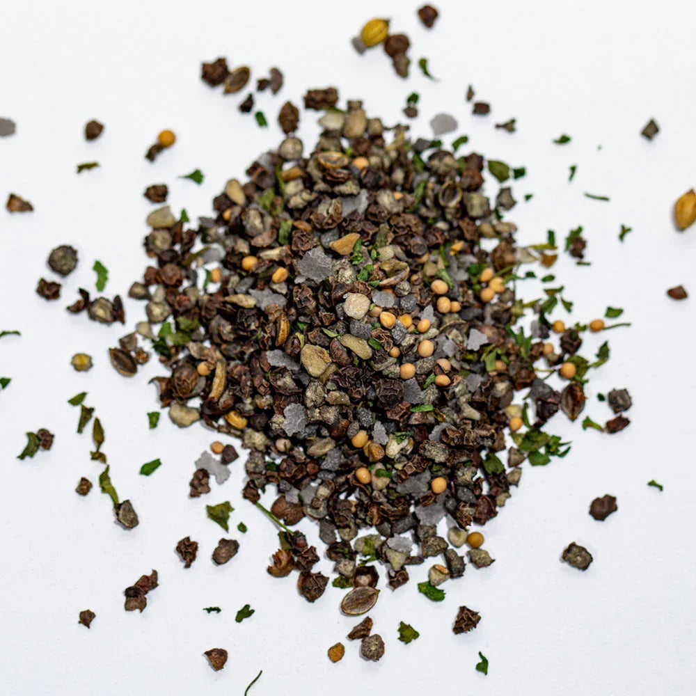 Coarse steak seasoning blend with peppercorns, mustard seeds, herbs on white background