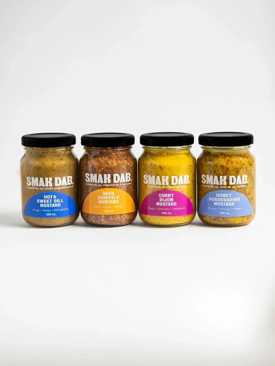 Four Smak Dab mustard jars—Hot & Sweet Dill, Beer Chipotle, Curry Dijon, Honey Horseradish—lined up on a white background.