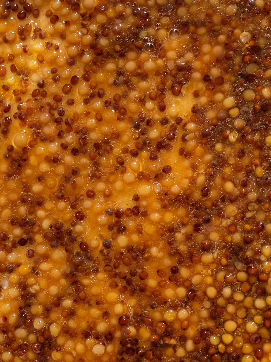 Close-up of whole grain mustard seeds in yellow mustard sauce