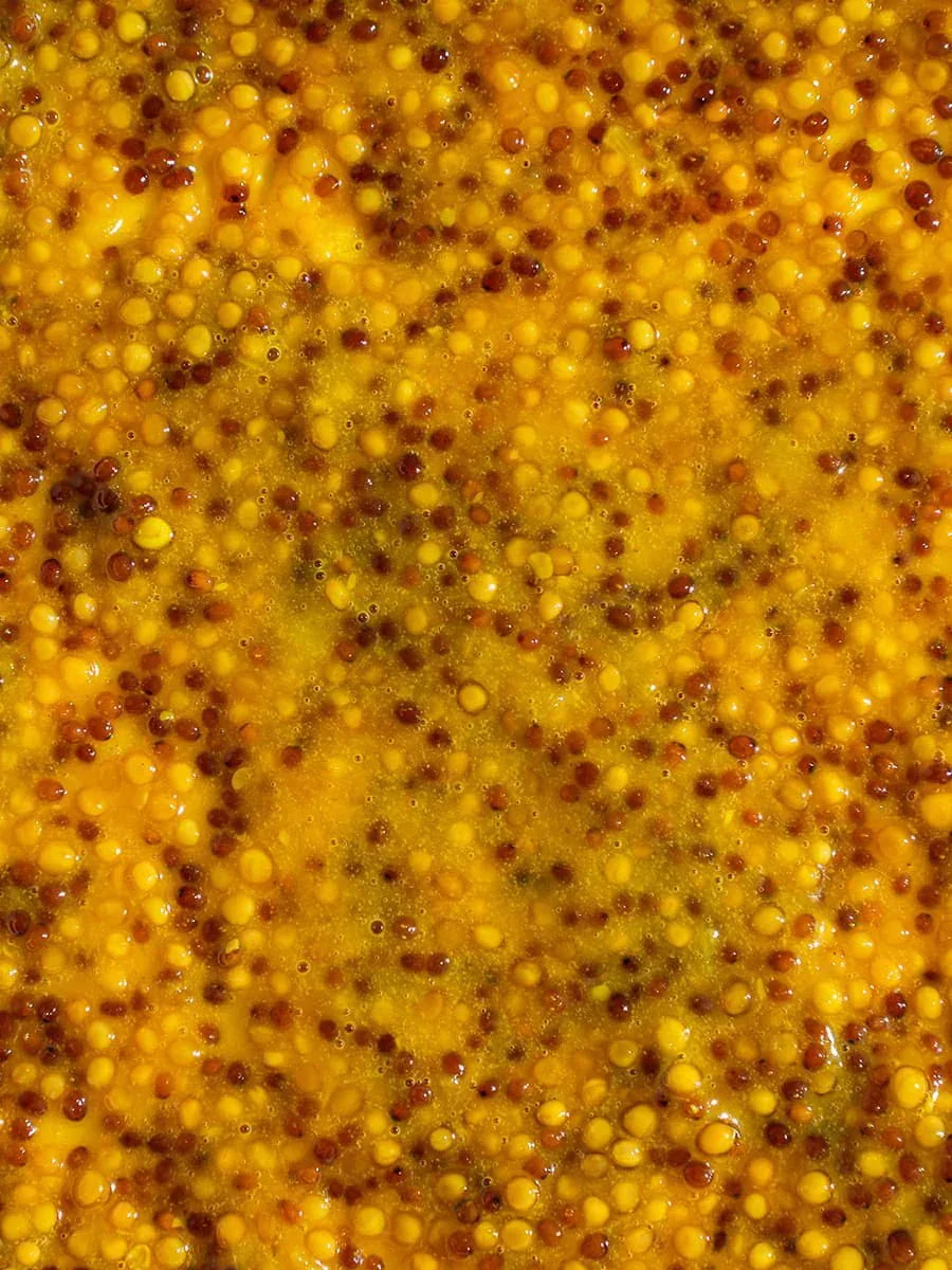 Close-up of whole grain yellow mustard seeds in a textured mustard sauce.