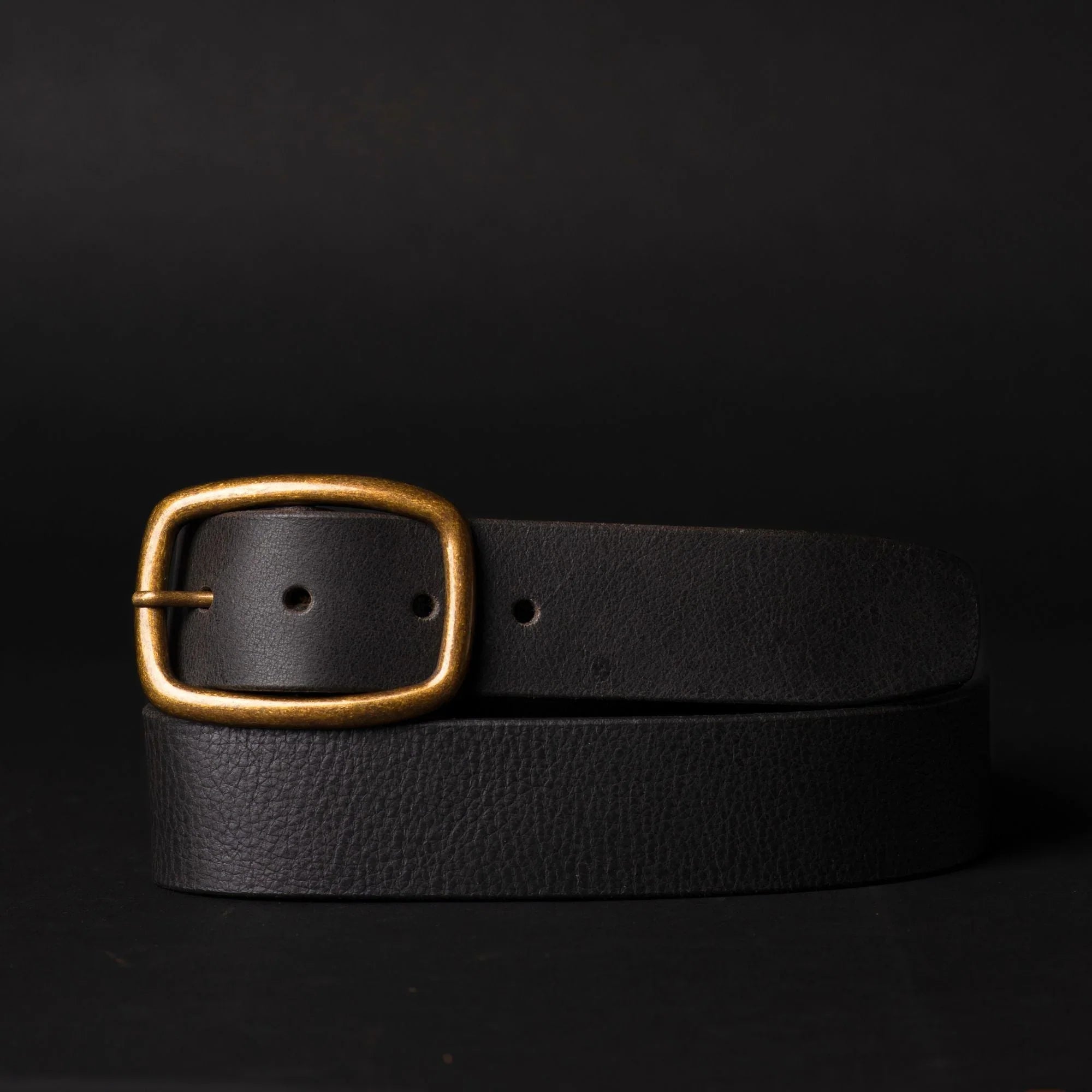Black leather belt with gold buckle on dark background