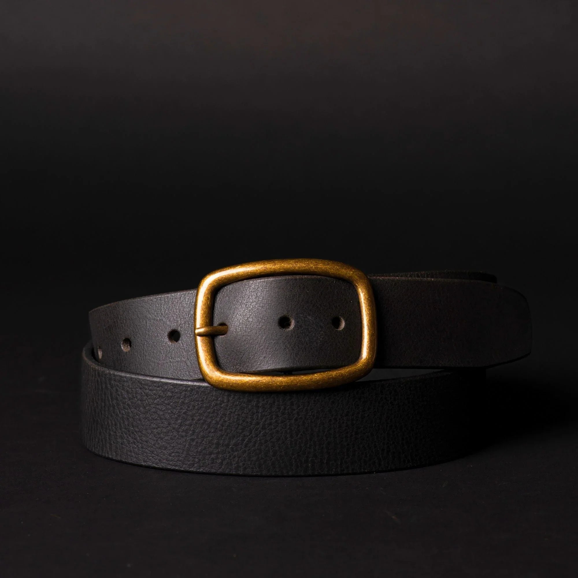 Black leather belt with gold buckle on dark background