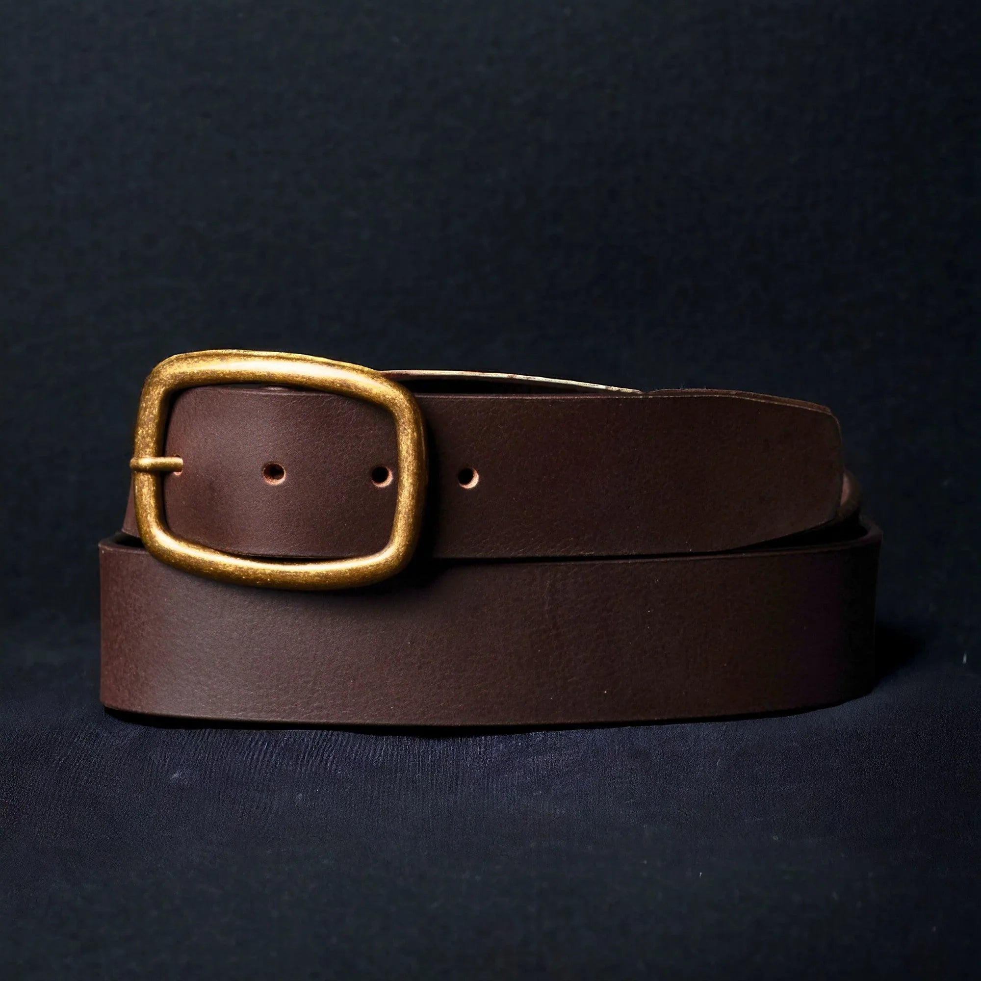 Handcrafted brown leather belt with gold brass buckle on dark background