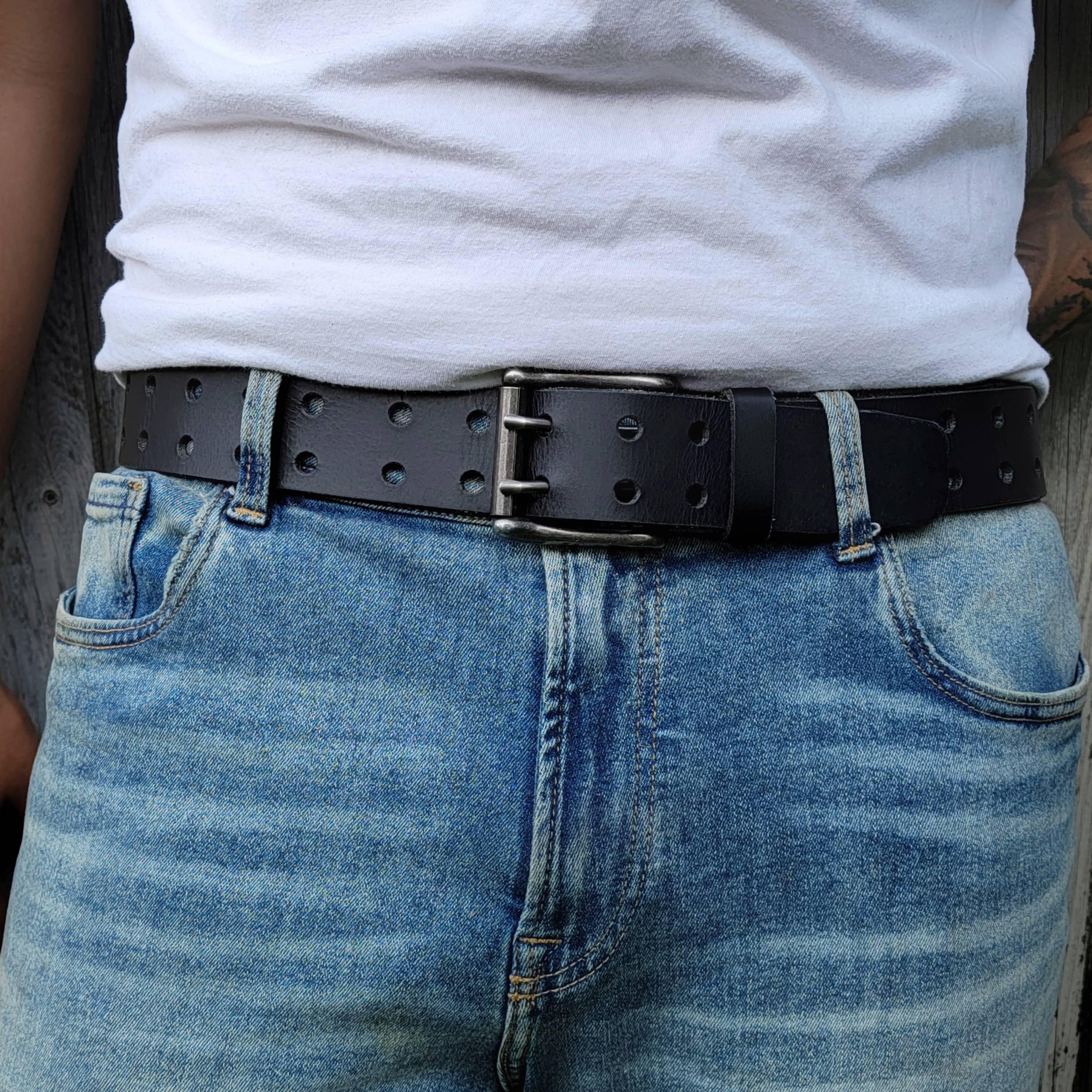 Black leather double prong belt with holes worn on blue jeans and white t-shirt