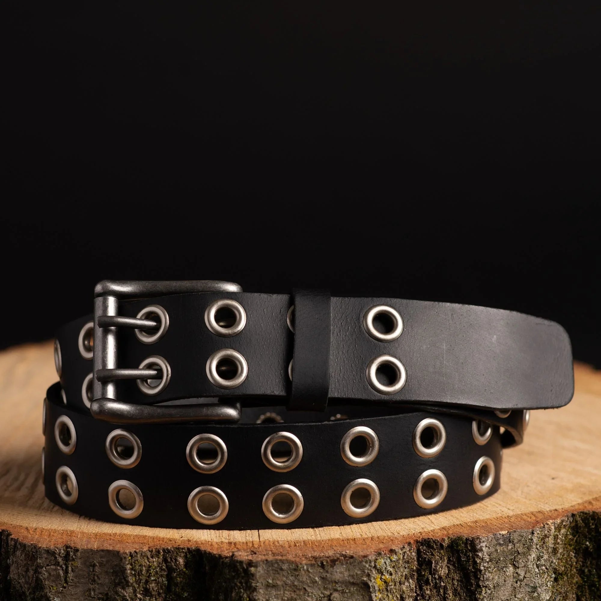Black leather grommet belt with silver holes on wood, punk fashion accessory