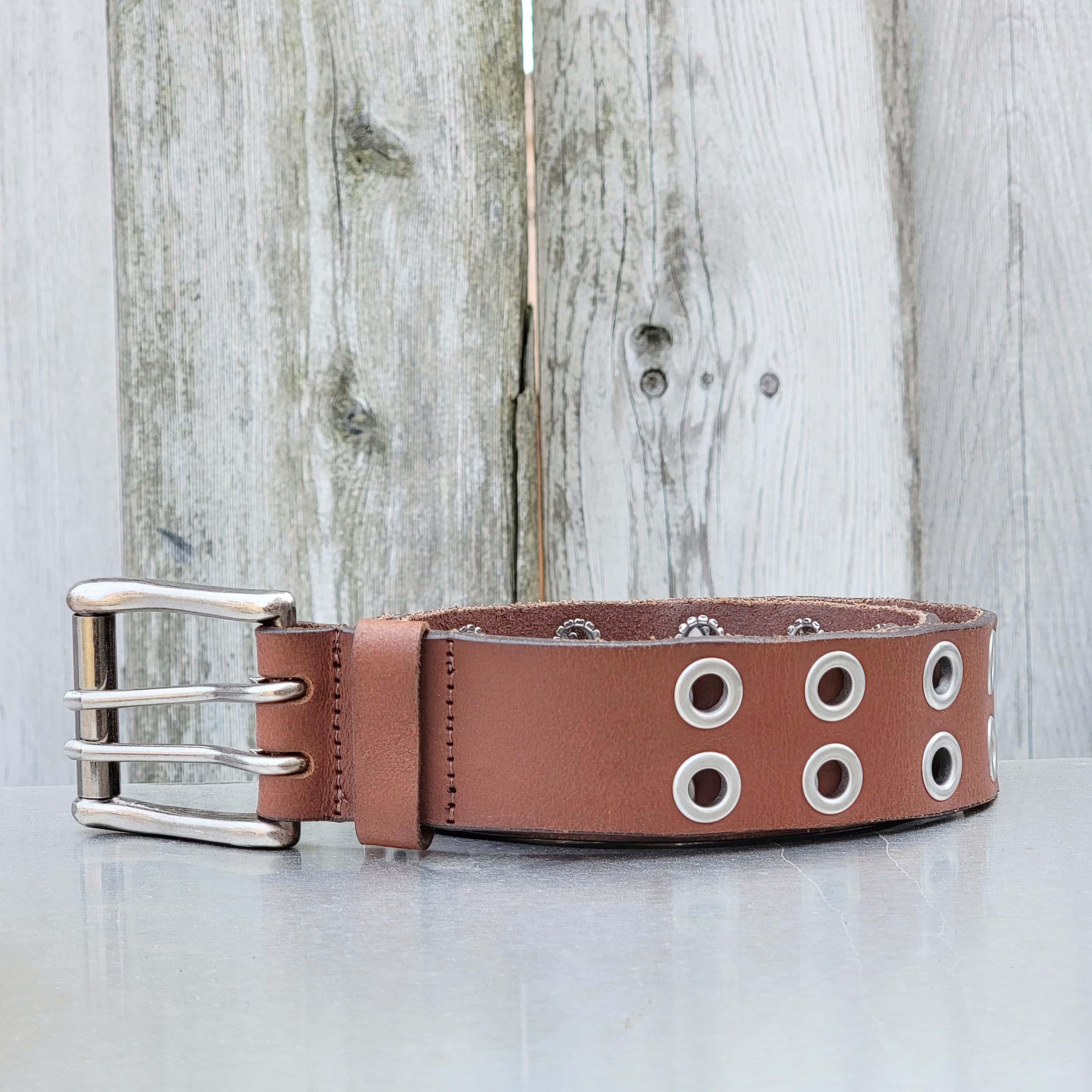 Brown leather grommet dog collar with double buckle on metal surface, wood background